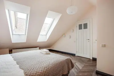 a white bedroom with a bed and two windows at 3 Bedroom Duplex Apartment next to the Gates of Dawn in Vilnius