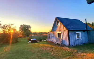 a small blue house in a field with the sunset at DAGNA summer house in Šunupis
