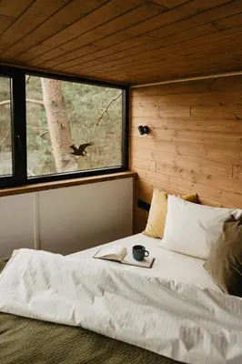 a bedroom with a bed with a book and a window at Treehouse Virš Bedugnės in Jurbarkas