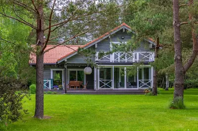 a gray house with a porch on a green lawn at Vila Shakti in Rudžionys
