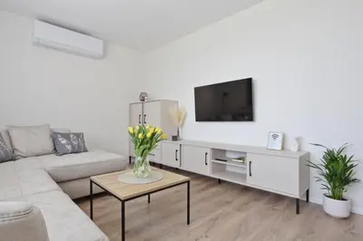 a white living room with a couch and a tv at Aušros apartamentai in Utena