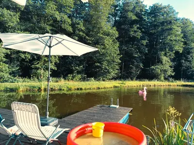 a table and chairs and an umbrella on a dock in a river at Reed Cottage in Dzenkuniskes