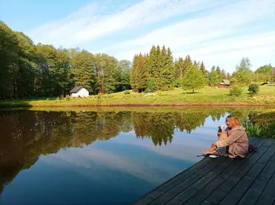 a woman sitting on a dock next to a lake at Reed Cottage in Dzenkuniskes