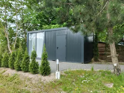 a gray building with a door and some trees at Šaltupio kaimo turizmas in Pakumprys