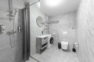 a bathroom with a shower and a sink and a washing machine at Stiklo Apartamentai in Radviliškis