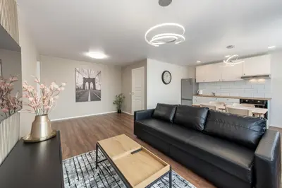 a living room with a black leather couch and a kitchen at Stiklo Apartamentai in Radviliškis