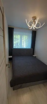 a bedroom with a bed with a chandelier and a window at Trumpalaikė apartamentų nuoma centre (Vytauto g.) in Šiauliai