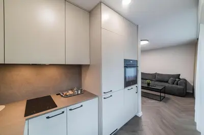 a kitchen with white cabinets and a living room at Frida Apartment in Šiauliai