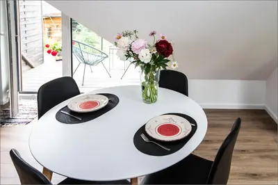 a white table with two plates and a vase of flowers at Rytas cozy apartment in the guest house with the terrace and the stunning view to the river side in Birštonas