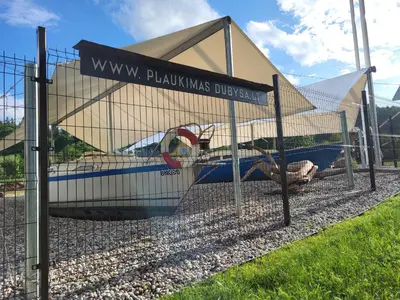 a fence with a boat in front of a building at Uždubysio baidarės Nakvynė Jachtose (Night on a Yacht) in Ariogala