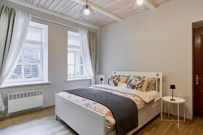a white bedroom with a bed and two windows at Cosy and authentic apartment in Vilnius Old Town in Vilnius