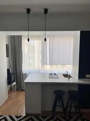 a kitchen with a white counter and two bar stools at Stilingi šaulio skulptūros apartamentai in Druskininkai