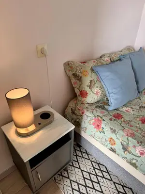 a bed with a night stand with a lamp on it at Rokiskis- jaukus butas su balkonu in Rokiškis
