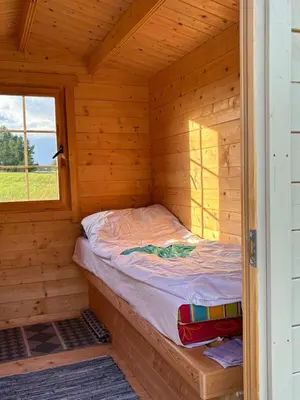 a small bed in a wooden cabin with a window at Bičių namas Bičių lova Bee house in Sargeliai
