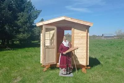 a woman standing in front of a wooden out house at Bičių namas Bičių lova Bee house in Sargeliai