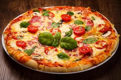 a pizza with tomatoes and basil on a plate on a table at Capsule Hostel Logistic Vilnius in Vilnius