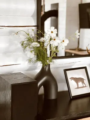 a black vase with white flowers on a table at HYTTE - Cozy Stay For Families & Friends in Jagėlonys Kalniniai