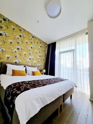 a bedroom with a large bed with a yellow wall at ALEGRE apartment in Druskininkai