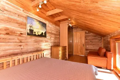 a bedroom in a log cabin with a bed and a chair at Bebrusų sodyba in Molėtai