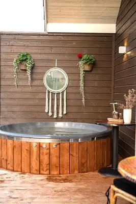 a hot tub in a room with a wooden wall at Milkės Karibai - poilsio namelis su sauna ir kubilu in Statiškė