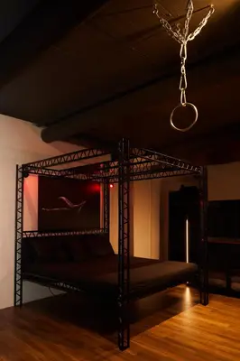 a black bed with a chain hanging from a ceiling at BDSM Black Apartments in Vilnius