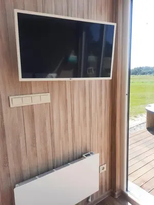 a tv on a wooden wall with a window at Vipoilsis Namelis N1 in Čekoniškės