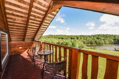 a balcony with chairs and a table and a view of a lake at Svajonių Dvaras in Balninkai