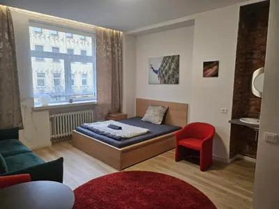 a small bedroom with a bed and a red chair at Kauno apartamentai Big room king size bed in Kaunas