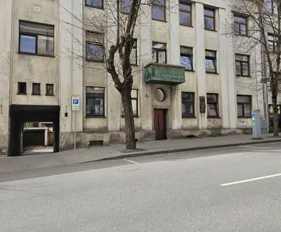 a building with a tree in front of a street at Kauno apartamentai Big bed in Kaunas