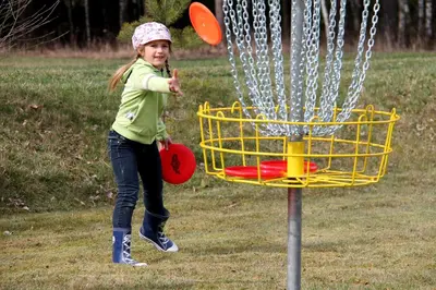 a young girl throwing frisbees into a yellow basket at Ramybės parkas in Sponėnai
