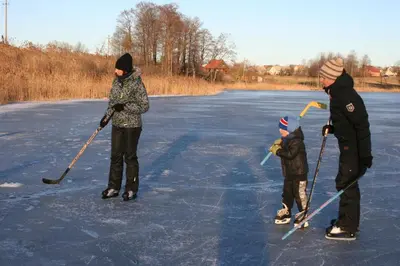two adults and a child playing hockey on the ice at Barškulių Sodyba in Ricieliai