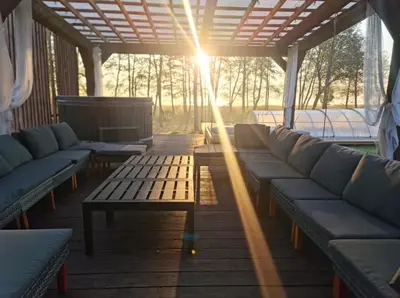 a porch with couches and a table with the sun shining at Poilsiaviete Vakaris in Gudeliai