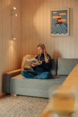 a woman sitting on a couch reading a book at Living art piece at the lake. in Užutrakis