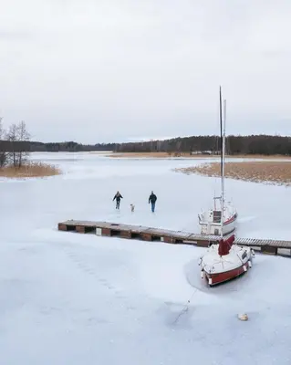 three people and a dog on a frozen lake with a boat at Living art piece at the lake. in Užutrakis
