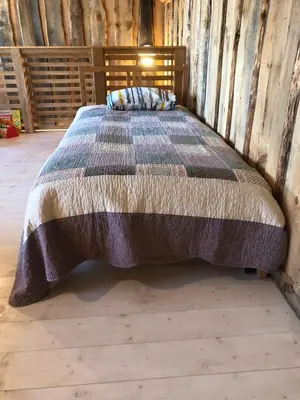 a bedroom with a bed with a blanket on it at Liepų pirtis in Smailiai