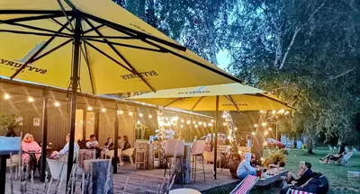 a group of people sitting at tables under umbrellas at Natur Camp Birštonas Small Cabins in Birštonas