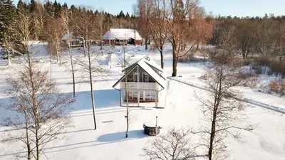 a small house in a snow covered field with trees at Namelis ant ežero kranto 