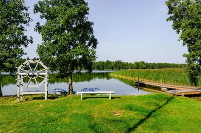 a white bench sitting on the grass next to a lake at Namelis ant ežero kranto 
