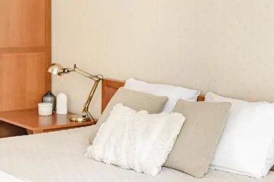 a bed with white pillows and a table with a lamp at Jacuzzi apartments x Free parking x SELF CHECK-IN 24x7 by H&H in Vilnius