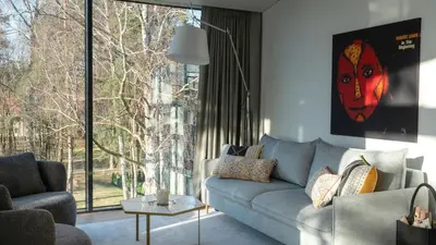 a living room with a couch and a large window at Butique Apartamentai Birštone - Holistic Skin & Wellness SPA Apartments - Inovatyvios dermatologijos centras in Birštonas