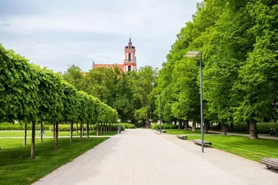 a walkway in a park with a clock tower in the background at Newly Refurbished Lukiskiu Square Apartment by Reside Baltic in Vilnius