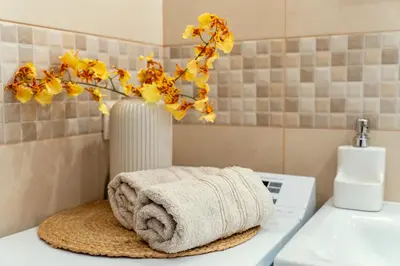 a bathroom with a towel and a vase with yellow flowers at Cozy Suite Roomita in Vilnius