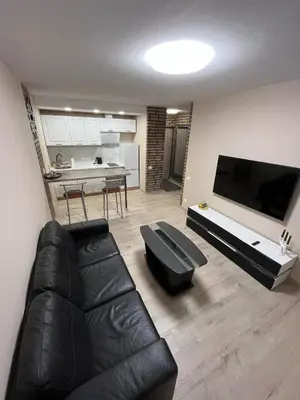 a living room with a black leather couch and a kitchen at Naujai įrengtas butas trumpalaikei nuomai in Šiauliai
