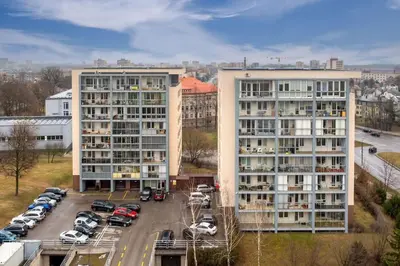 two tall apartment buildings with cars parked in a parking lot at Apartment with cozy balcony by URBAN RENT in Kaunas