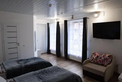 a bedroom with two beds and a chair and a television at Svečių namai Aurėja in Kėdainiai