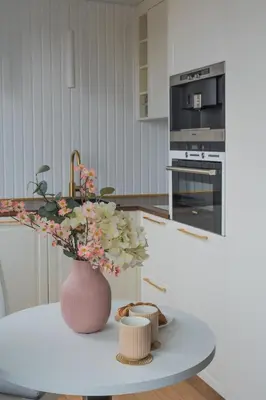 a white kitchen with a vase with flowers on a table at Old Town view Apartment in city center in Anykščiai