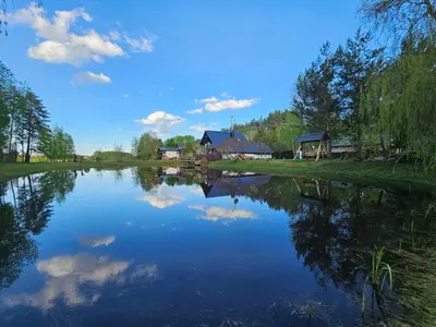 a river with a reflection of a house in the water at Pakalnės sodyba in Skverbai