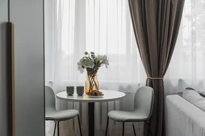 a vase of flowers on a table in front of a window at City Center Apartment with balcony in Anykščiai