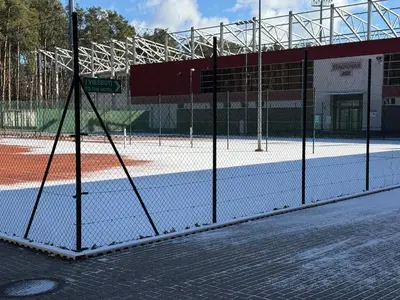a tennis court with a fence in front of a building at Alytaus sporto viešbutis Self Check-in in Alytus