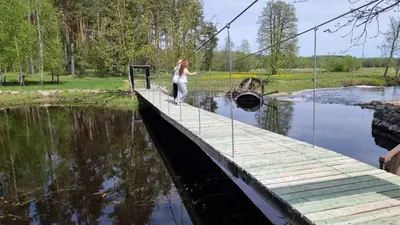 a woman walking across a bridge over a river at Pakalnės sodyba in Skverbai